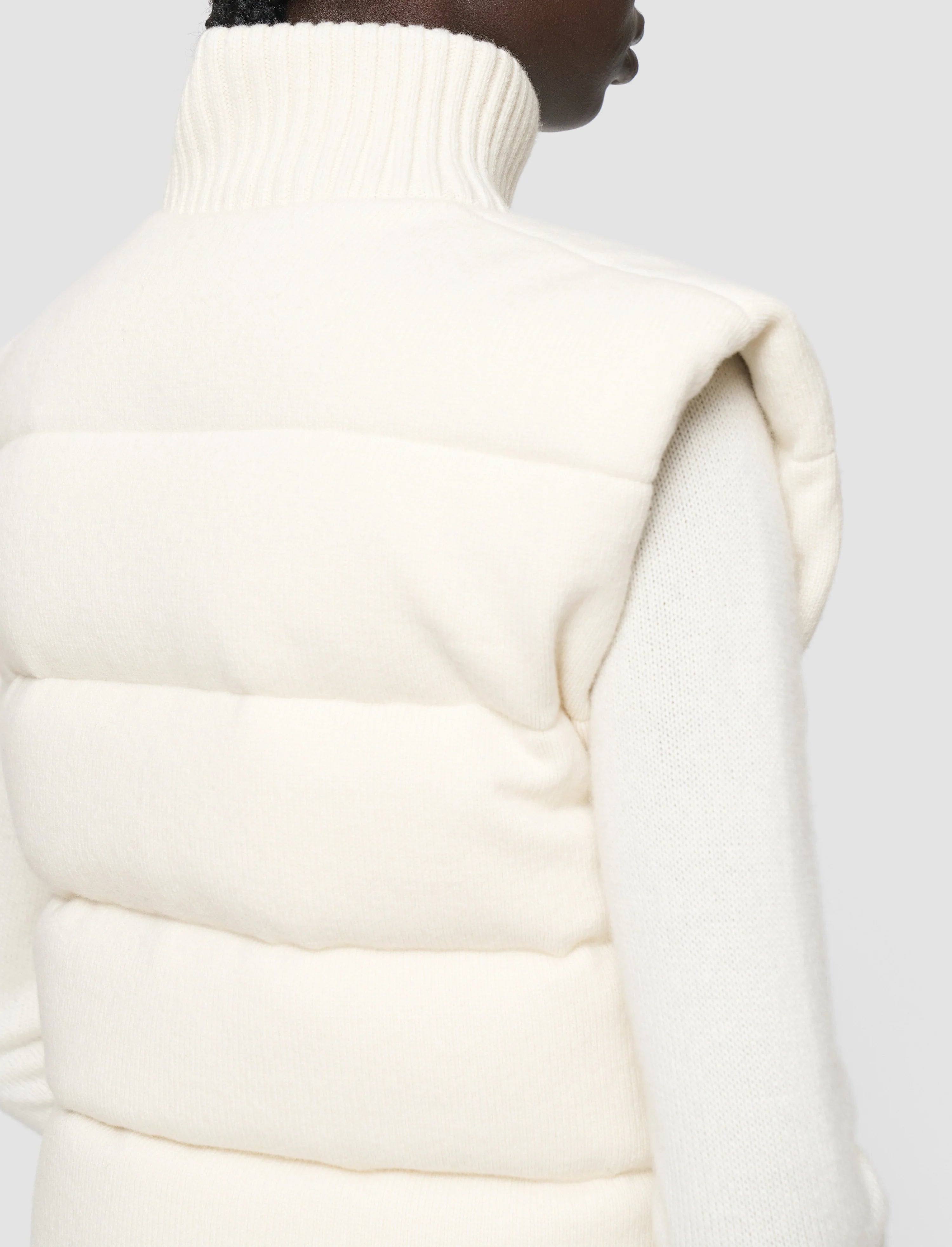 Close-up of a person wearing a white puffer vest against a light gray background