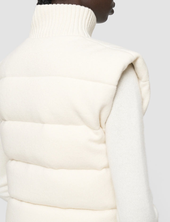 Close-up of a person wearing a white puffer vest against a light gray background