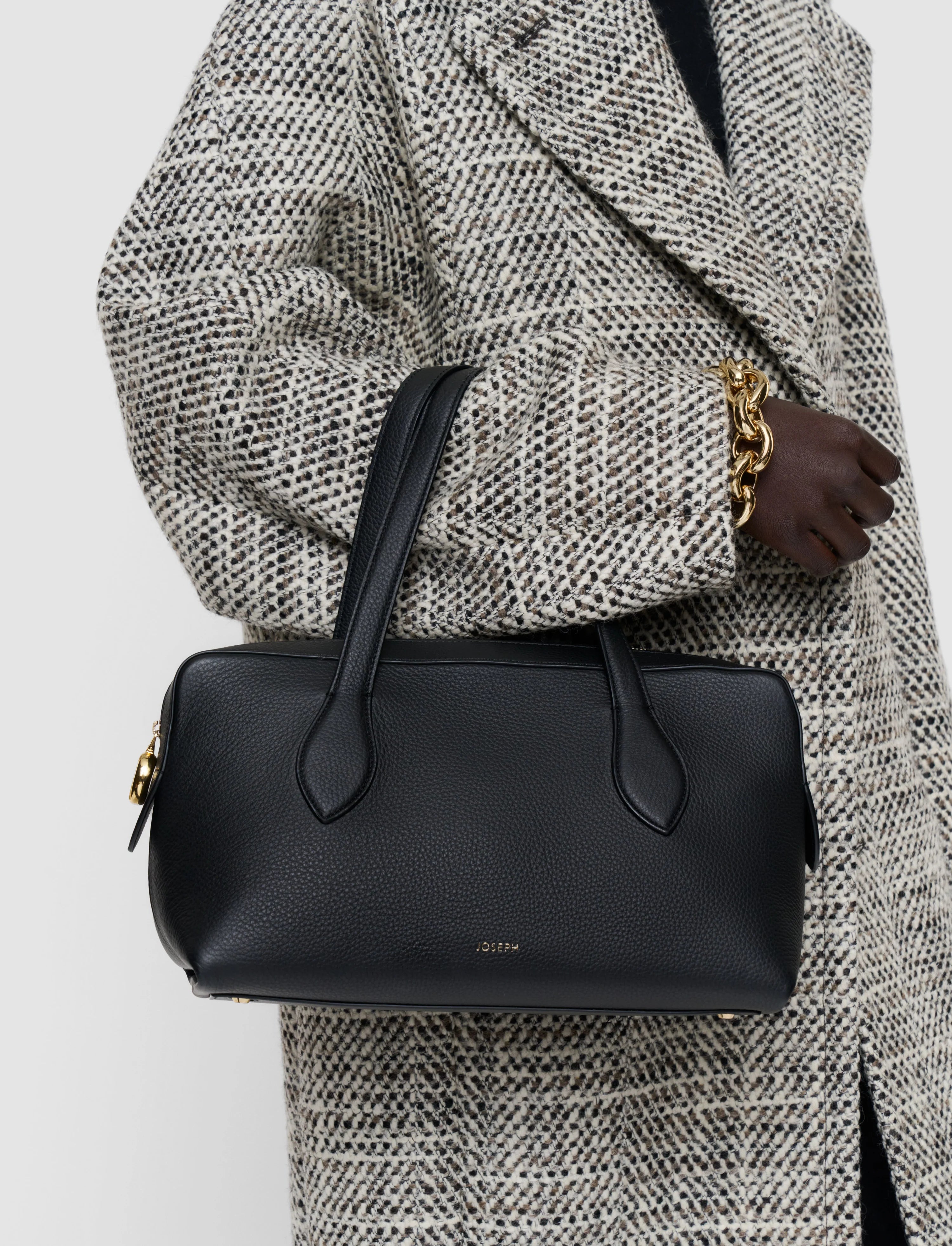 Person wearing a textured coat holding a black handbag with a visible brand logo.