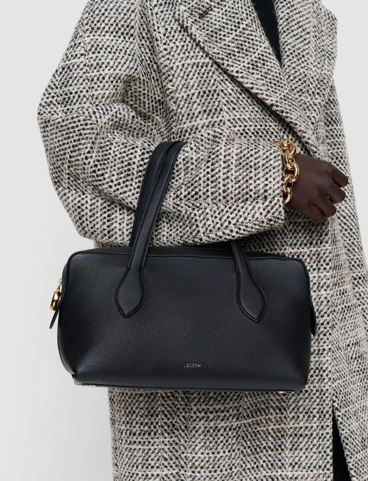 Person wearing a textured coat holding a black handbag with a visible brand logo.