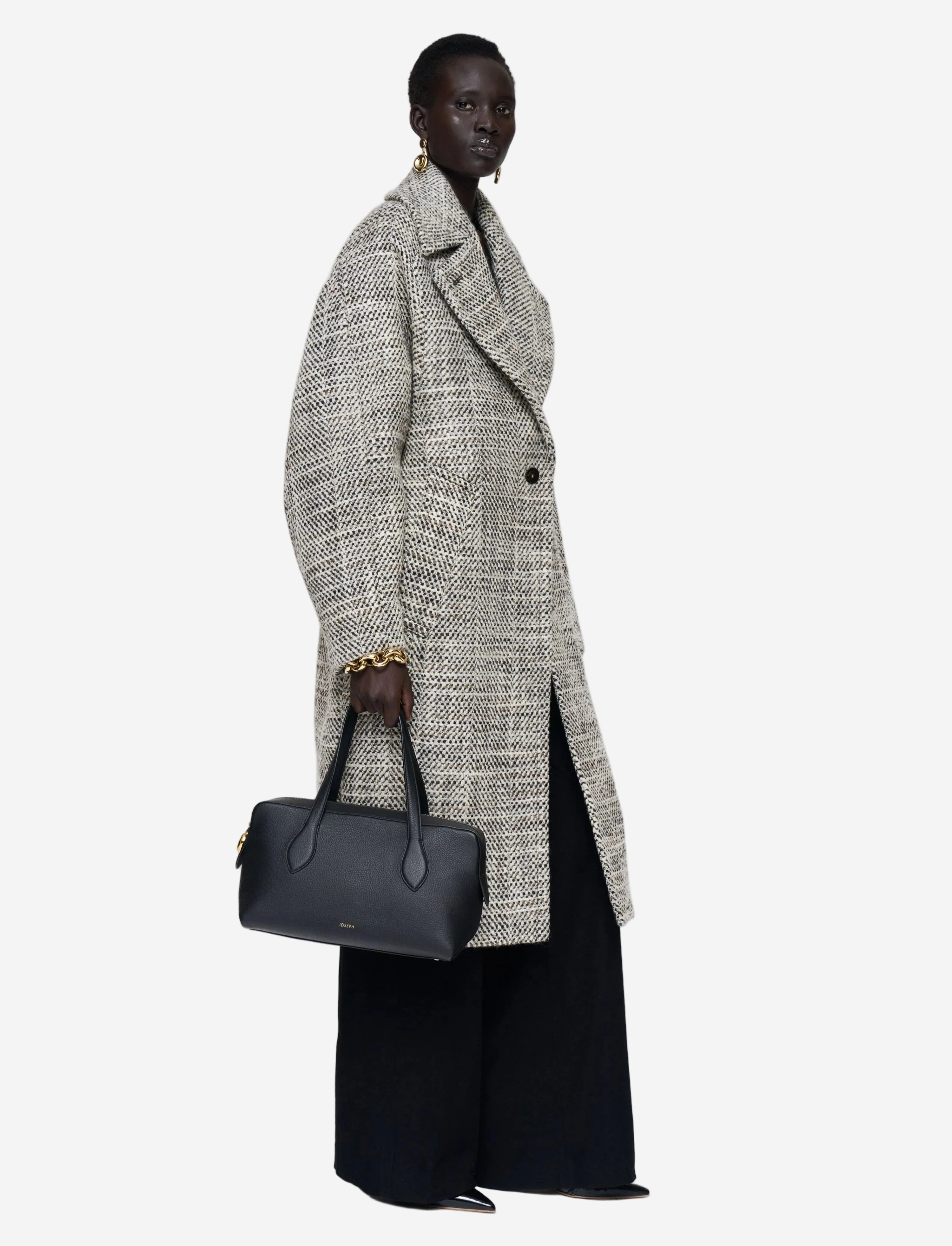Person wearing a long, patterned coat holding a black handbag on a white background