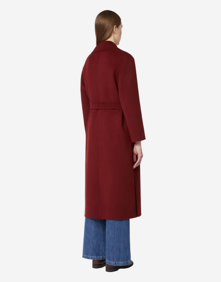 Person wearing a long burgundy coat and blue jeans on a white background
