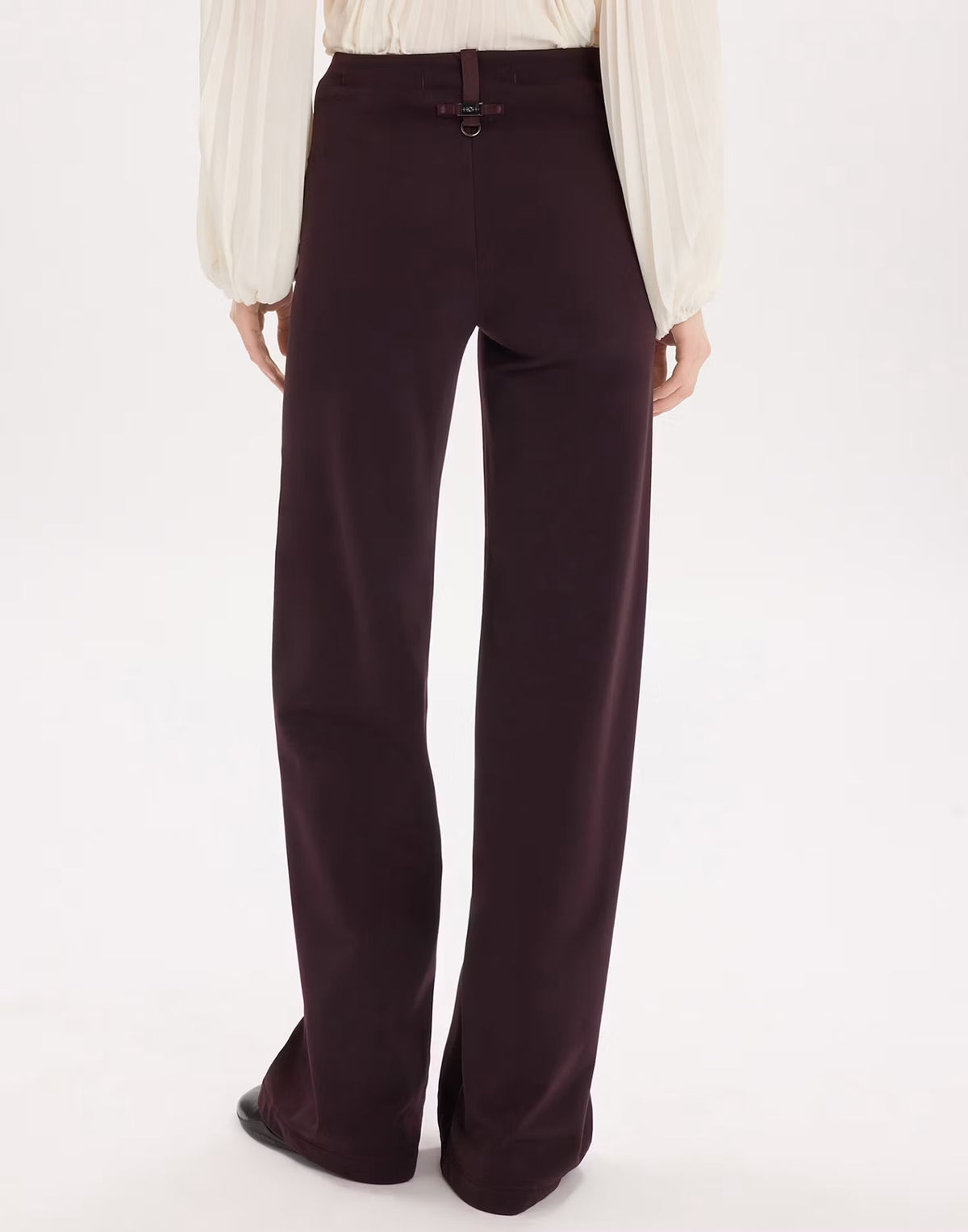 A person shown from the back wearing dark plum wide-leg trousers and a cream blouse against a plain white studio background.