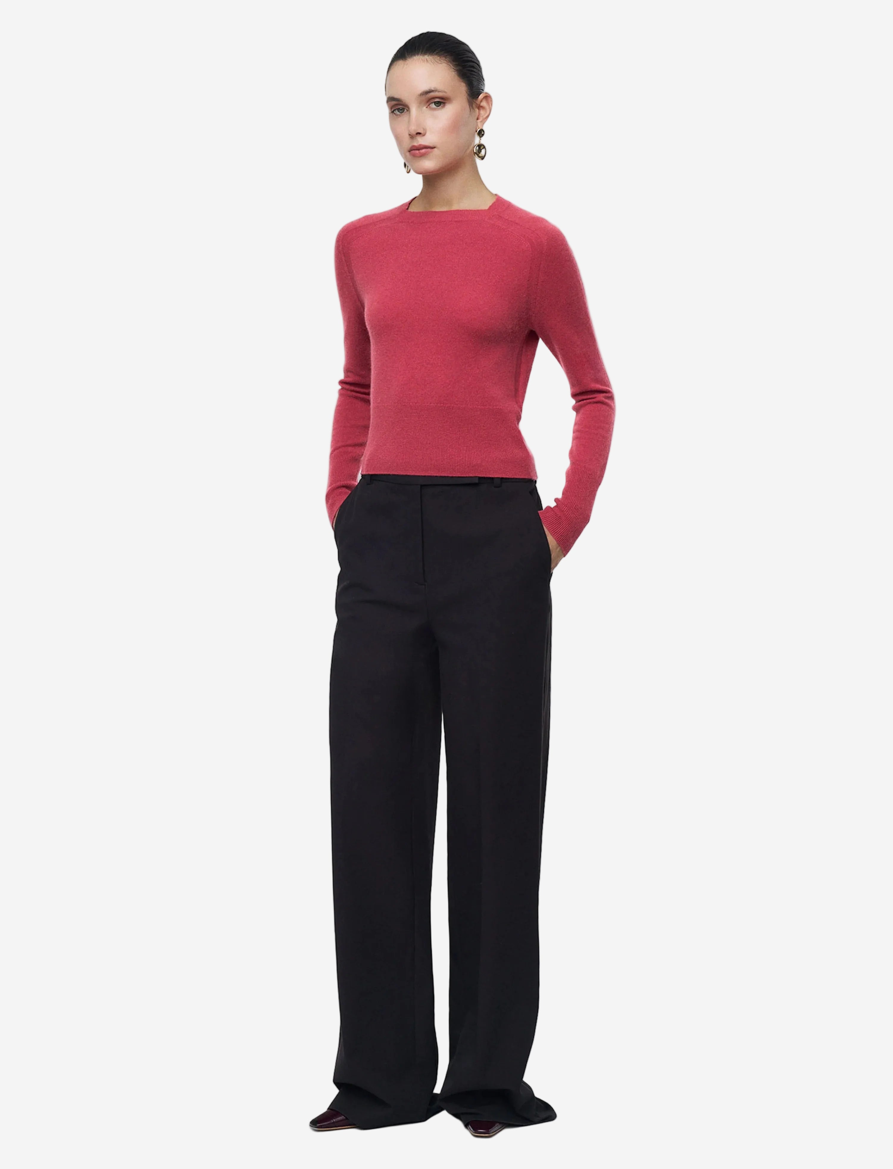 Woman wearing a red sweater and black pants on a light gray background
