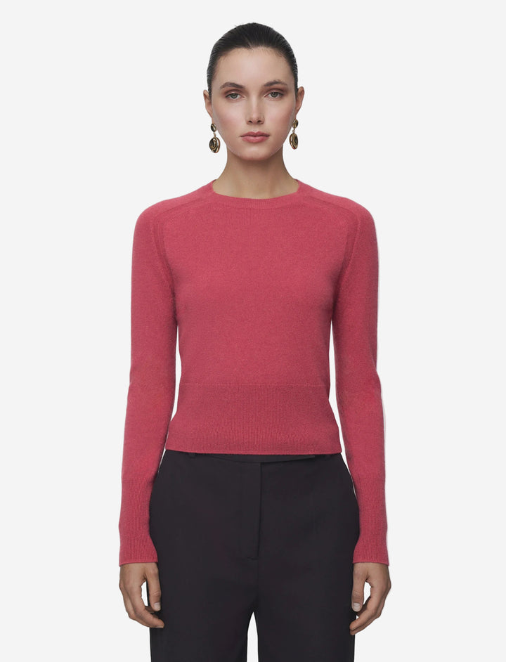 Woman wearing a pink sweater and black pants on a gray background