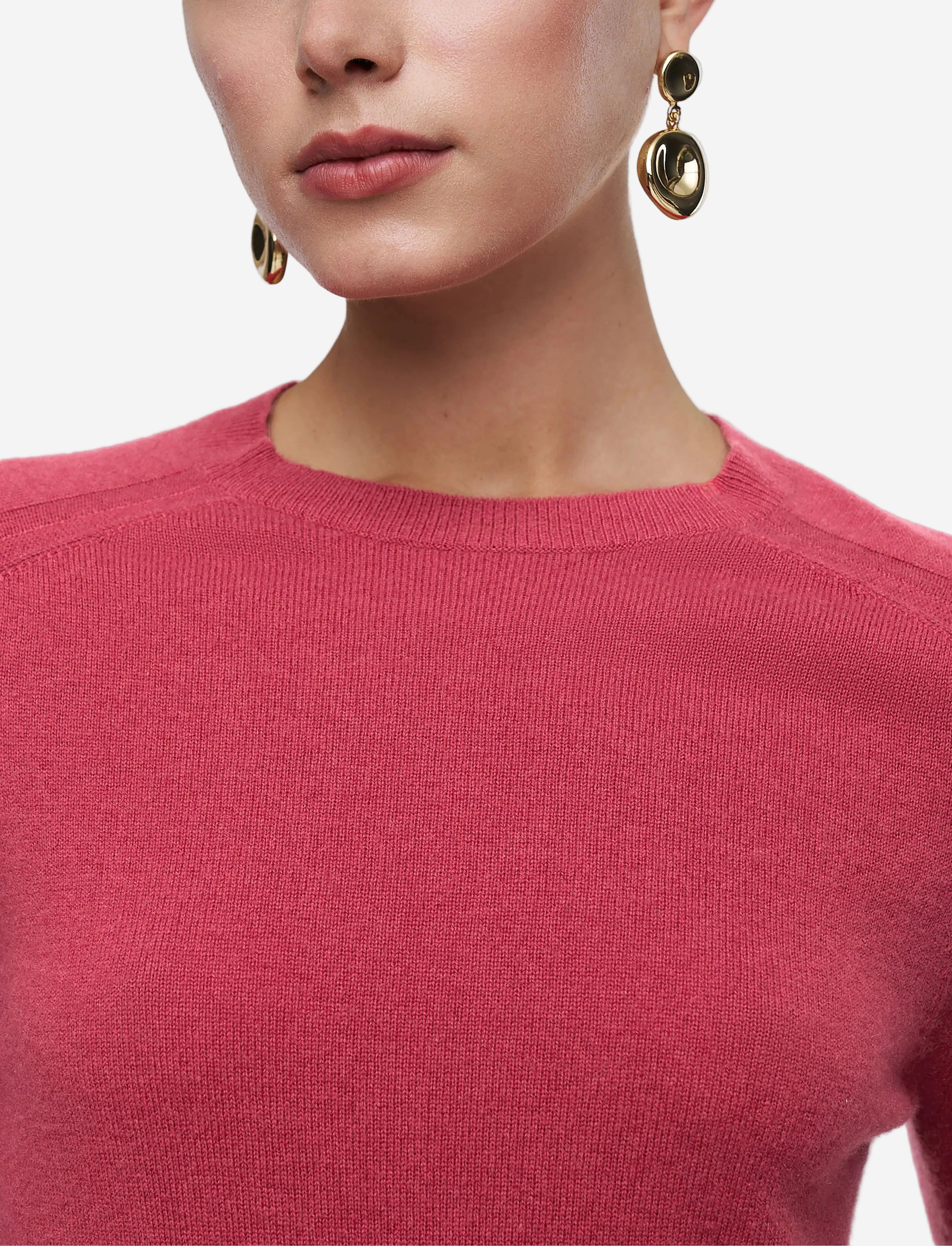Person wearing a pink sweater with gold earrings on a light gray background