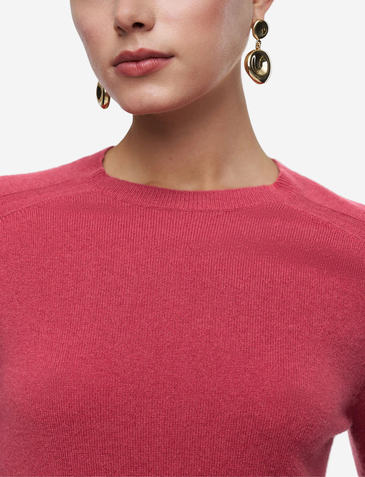 Person wearing a pink sweater with gold earrings on a light gray background