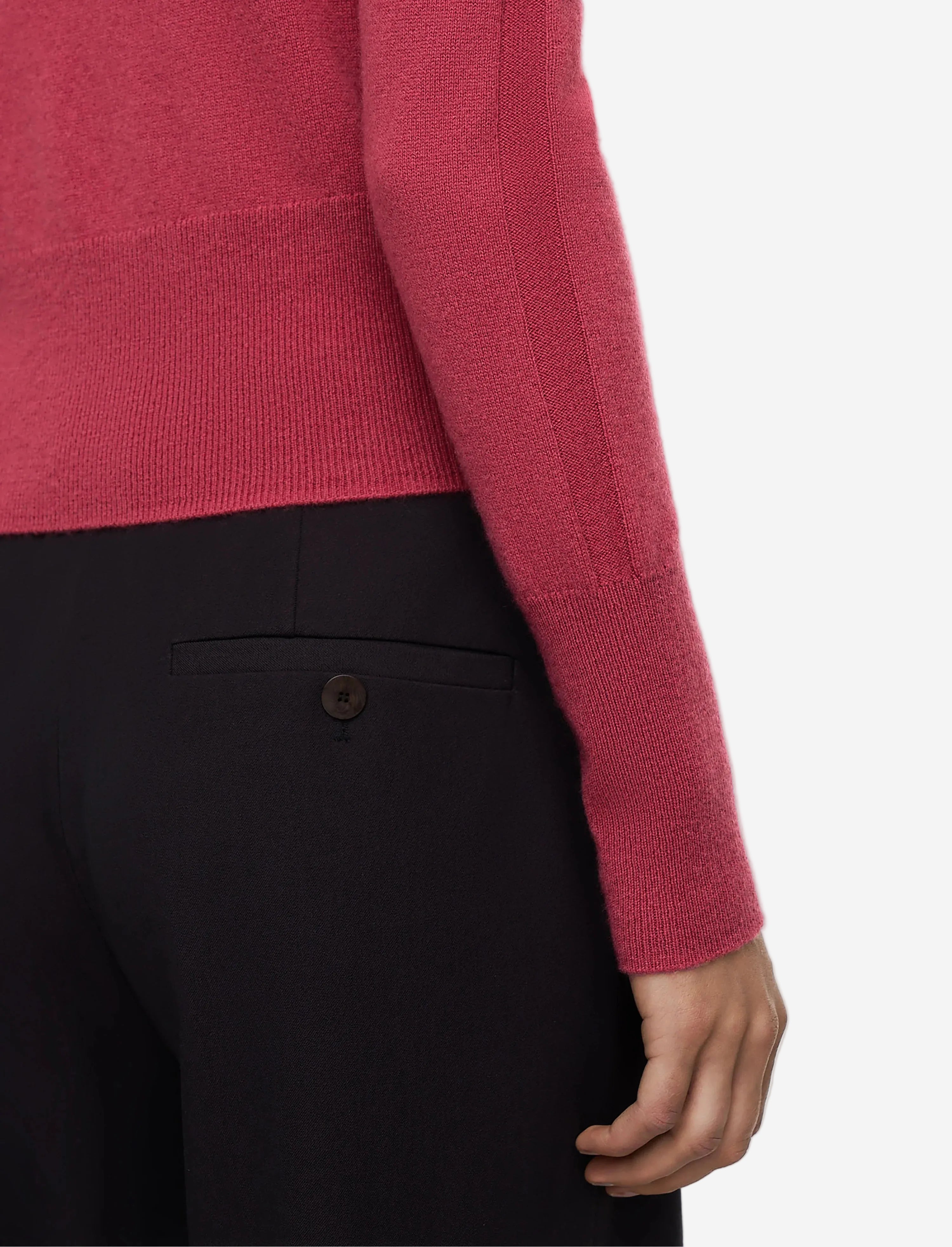 Close-up of a person wearing a pink sweater and black pants on a light gray background