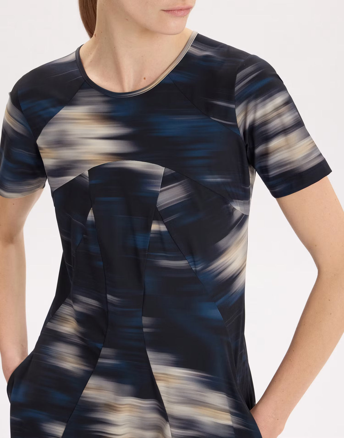 A close-up of a model wearing a short-sleeve tunic top with an abstract, painterly brushstroke pattern in navy blue, black, beige, and white.