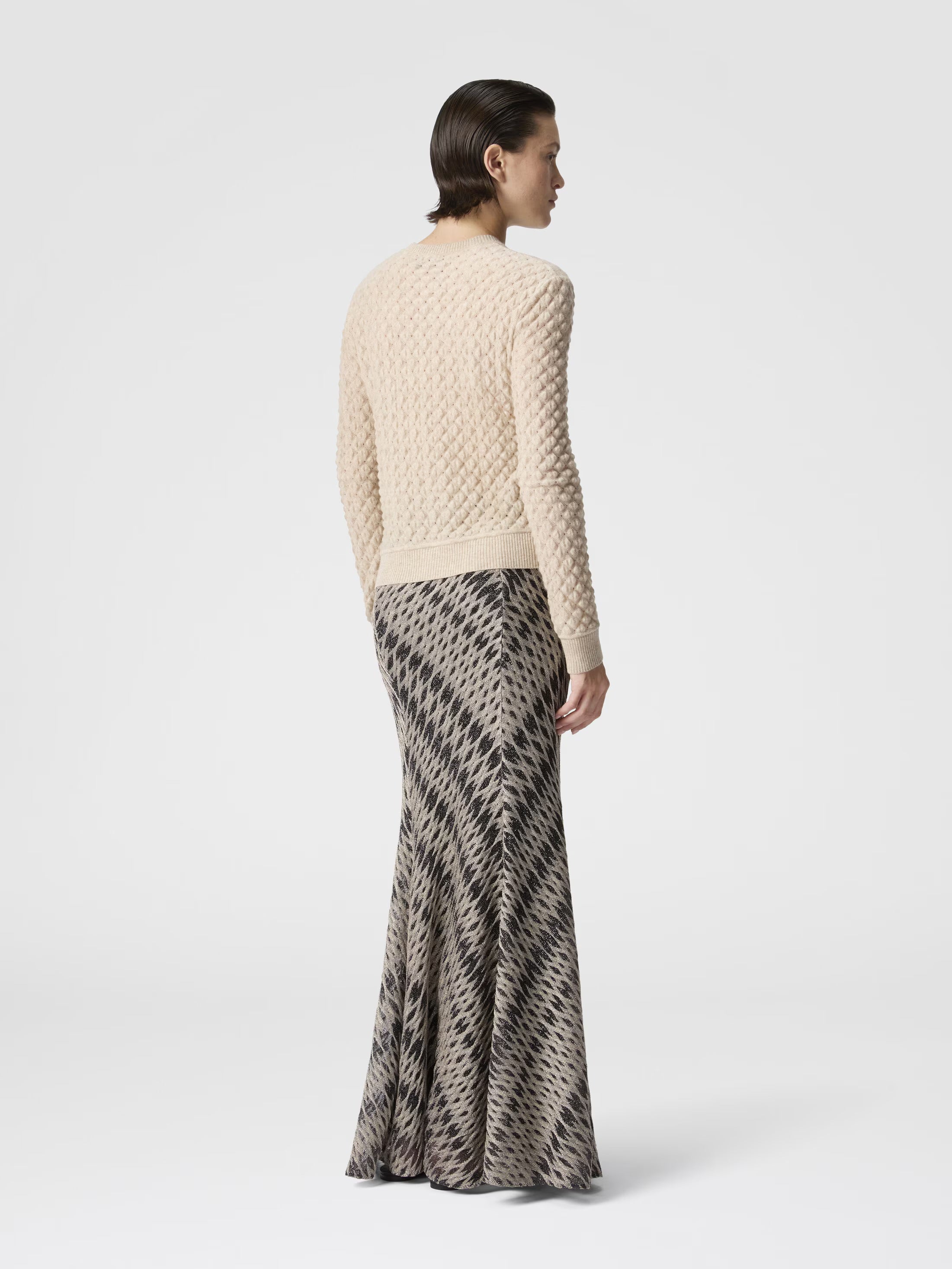 Woman wearing a textured beige sweater and patterned skirt on a white background