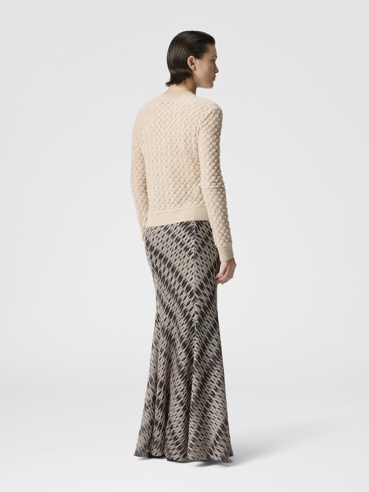 Woman wearing a textured beige sweater and patterned skirt on a white background