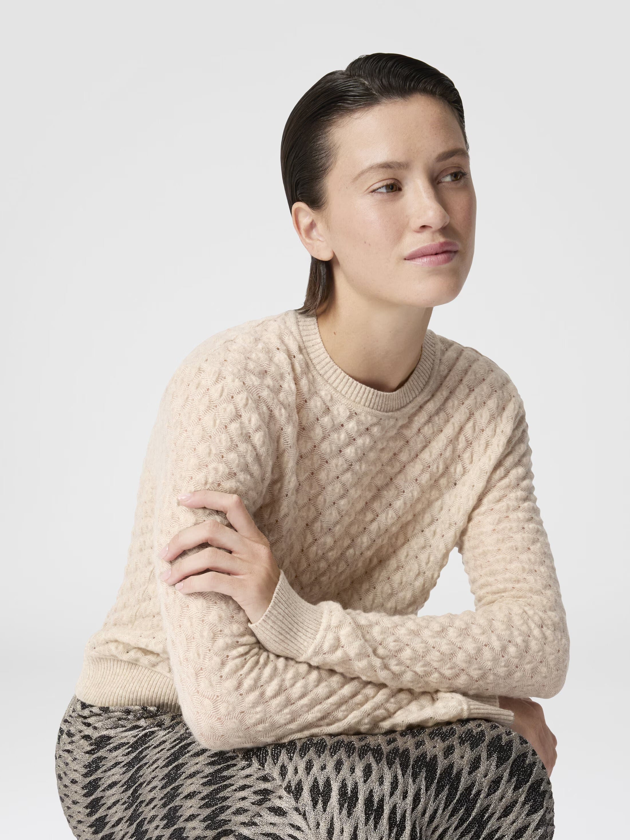 Woman wearing a beige cable knit sweater against a plain background