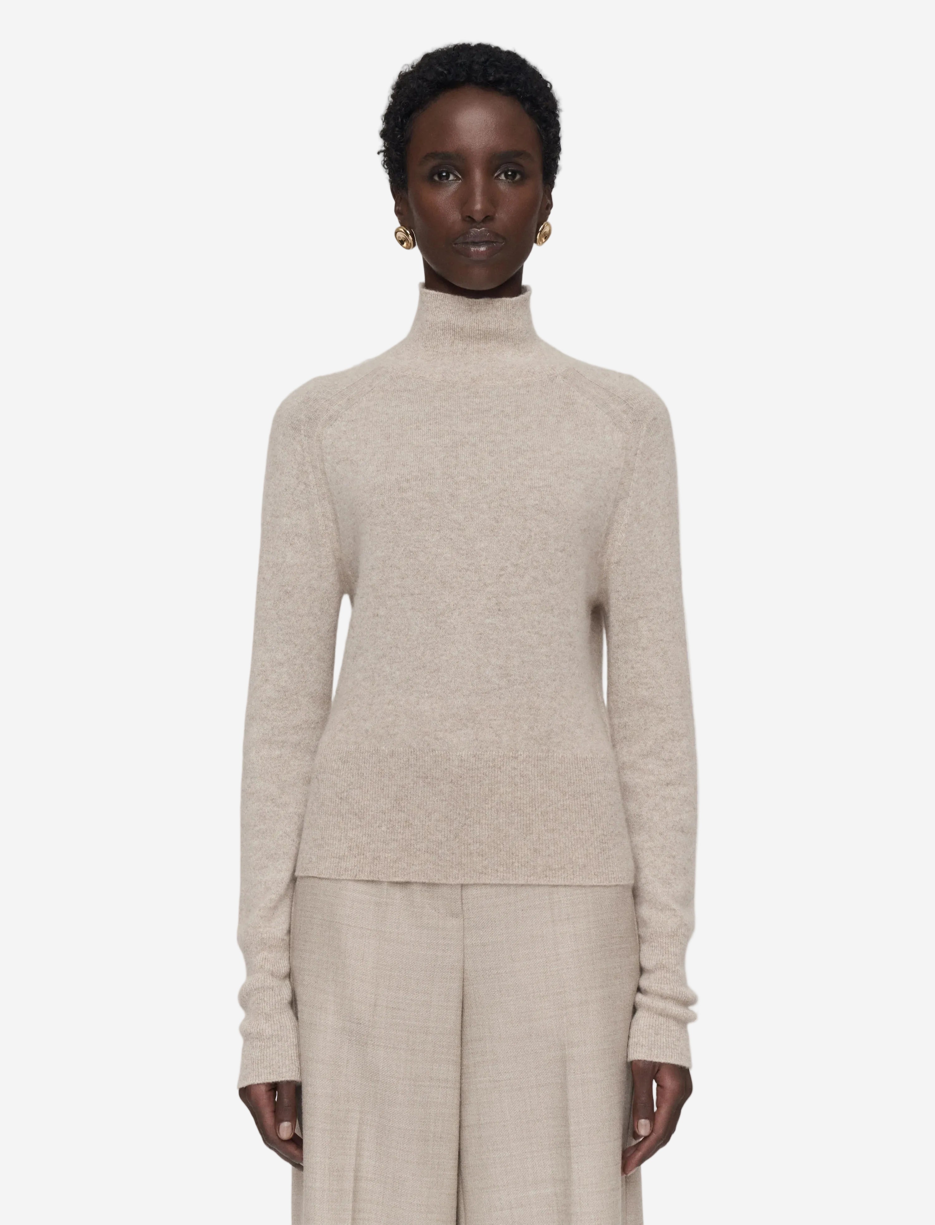 Person wearing a beige turtleneck sweater and pants on a white background