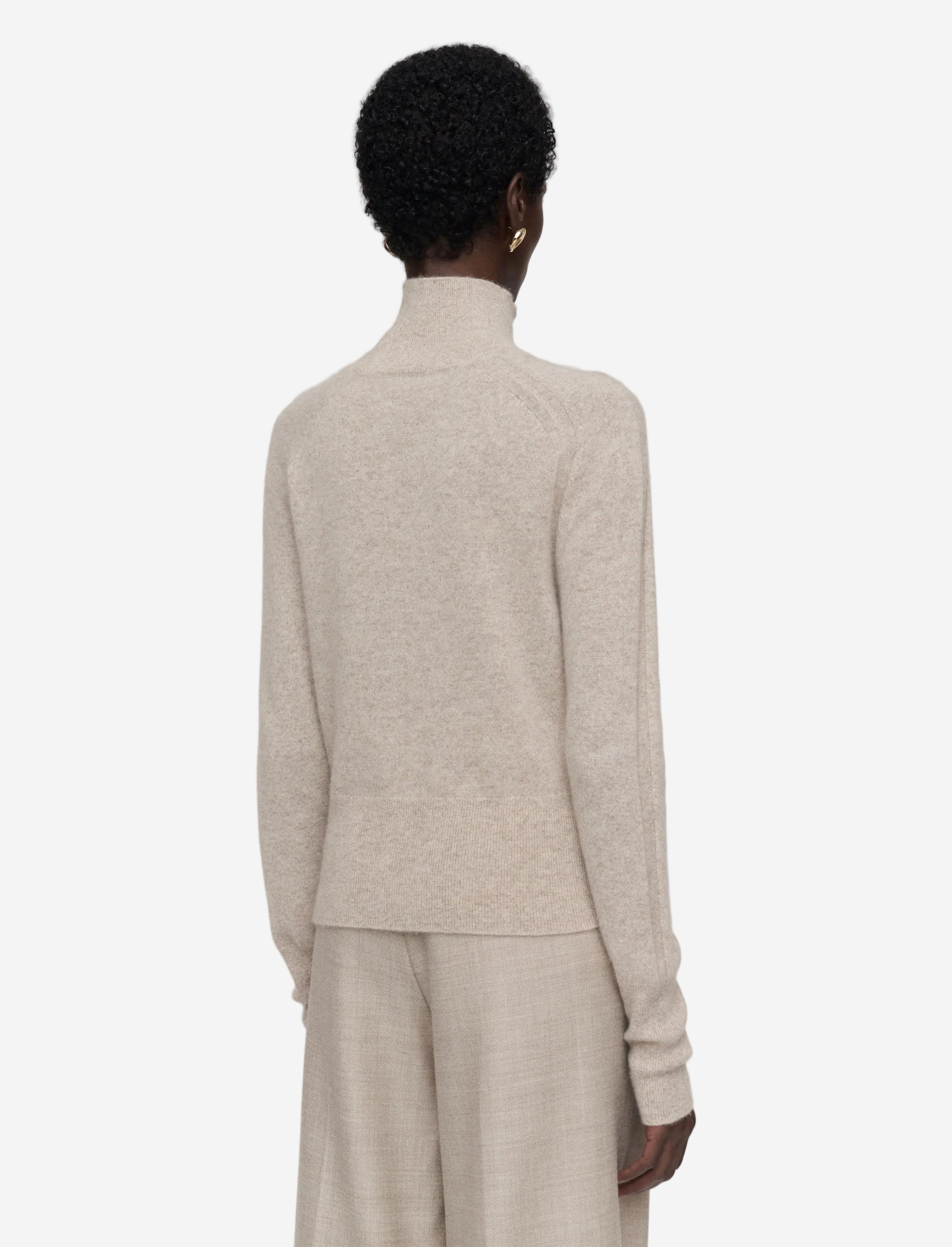 Person wearing a beige sweater and pants set on a light gray background