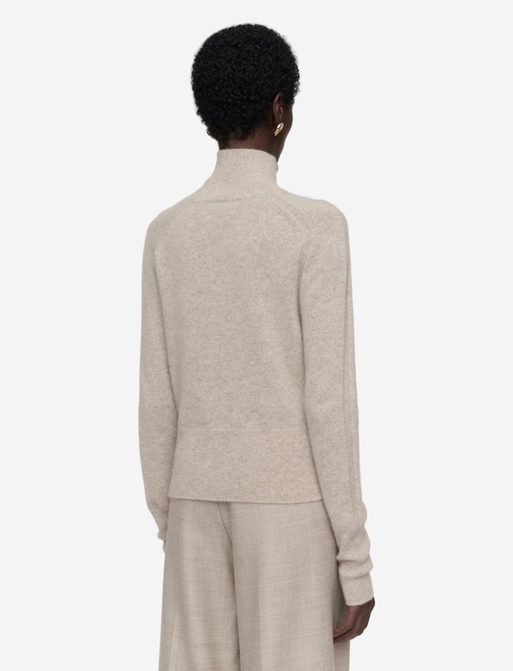 Person wearing a beige sweater and pants set on a light gray background