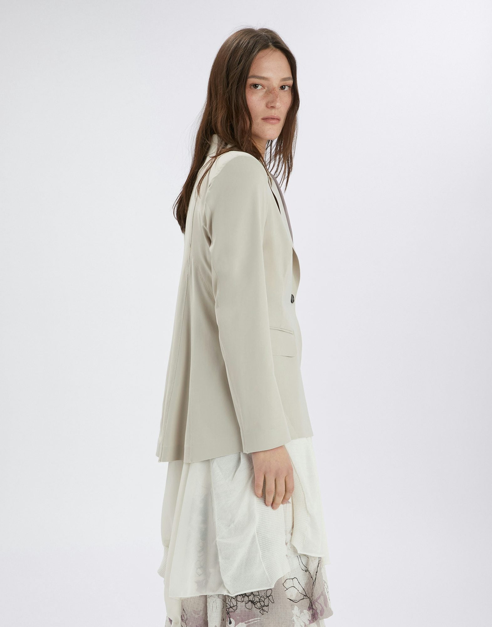 Woman wearing a light-colored blazer over a white dress on a white background
