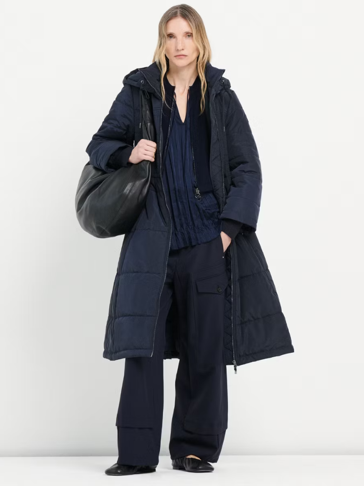 Person wearing a long navy coat holding a black bag on a white background