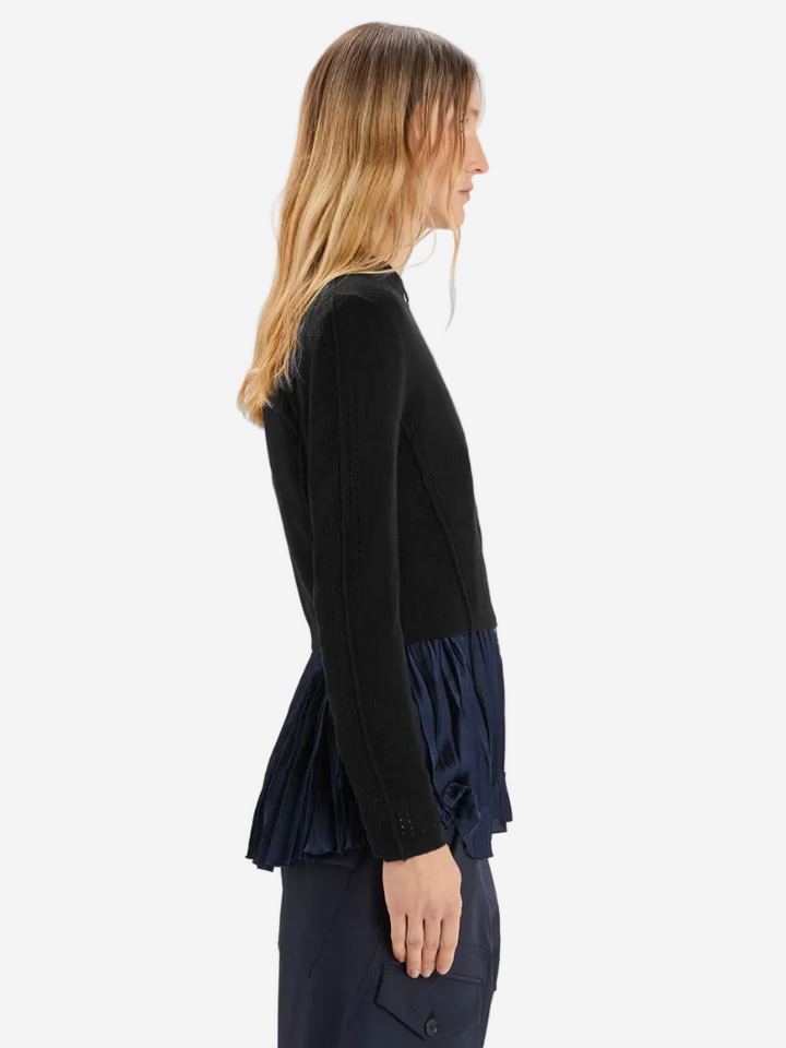 Woman wearing a black long-sleeve top with a navy blue peplum detail on a white background