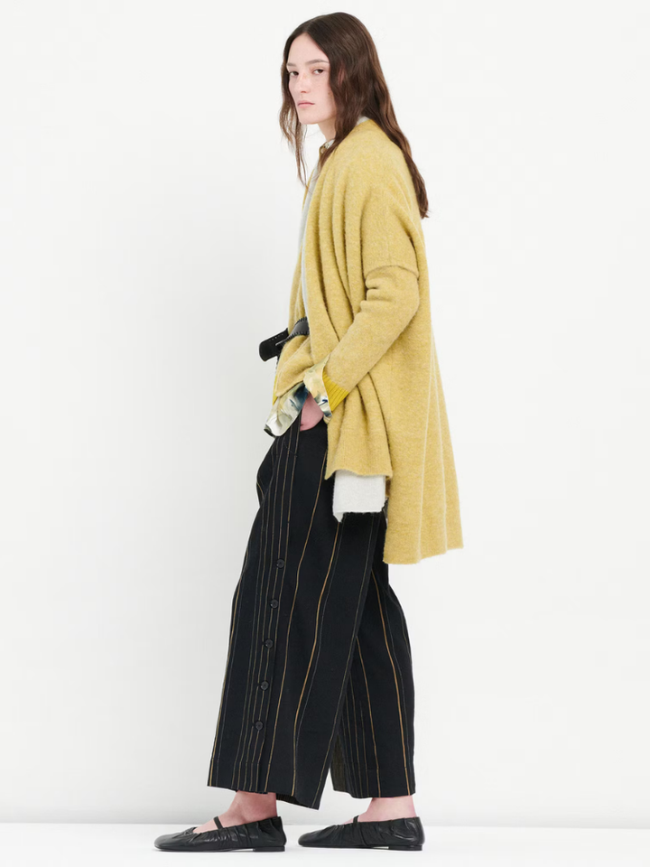 Person wearing a mustard yellow cardigan and black pinstripe pants on a white background