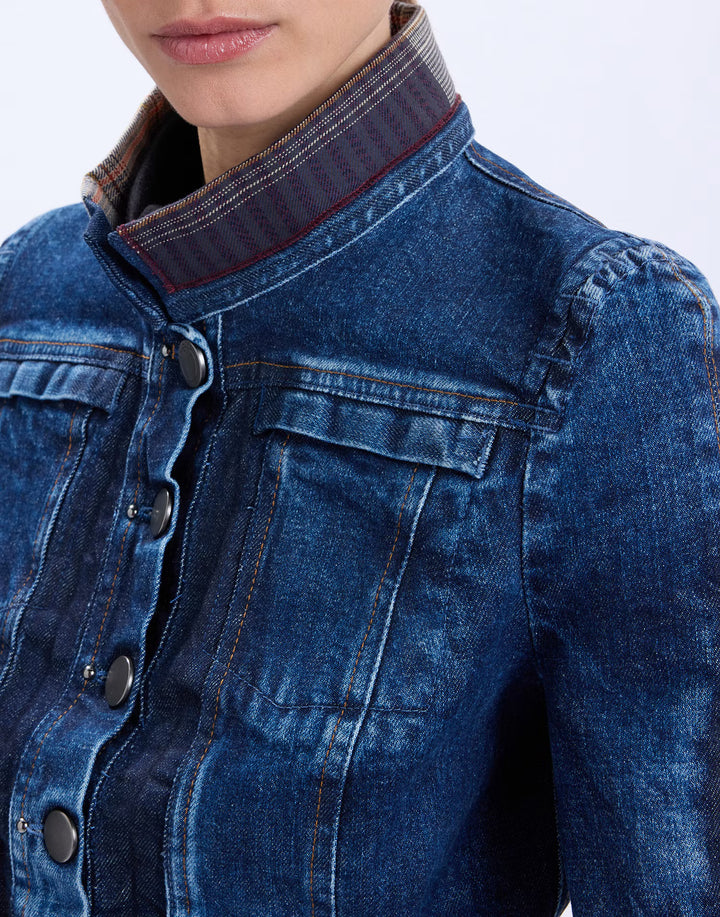 Close-up of a person wearing a dark blue denim jacket with a high ribbed collar and dark buttons, against a plain light background.