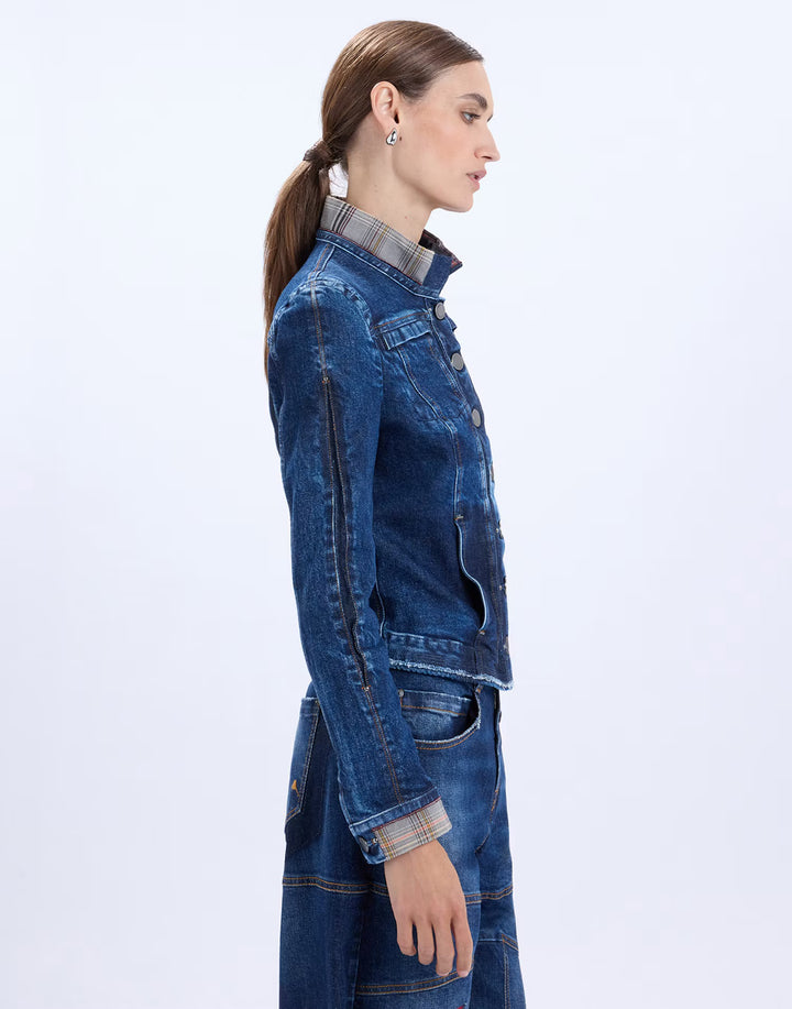 A woman in side profile wearing a dark blue denim jacket with a plaid collar, photographed against a clean white studio background.