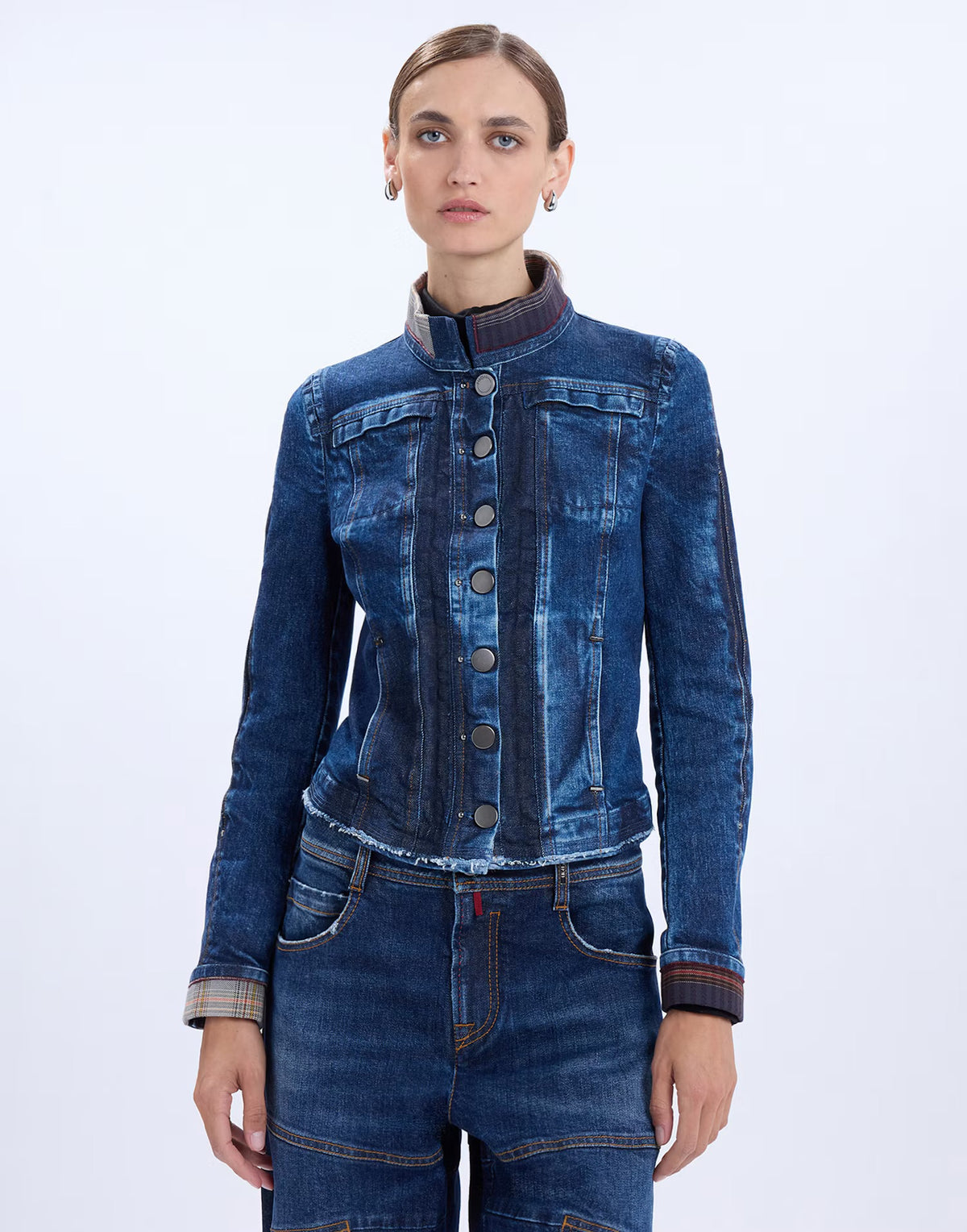 A model wearing a dark blue denim jacket with a mandarin collar and button front, paired with matching blue jeans, against a plain white studio background.