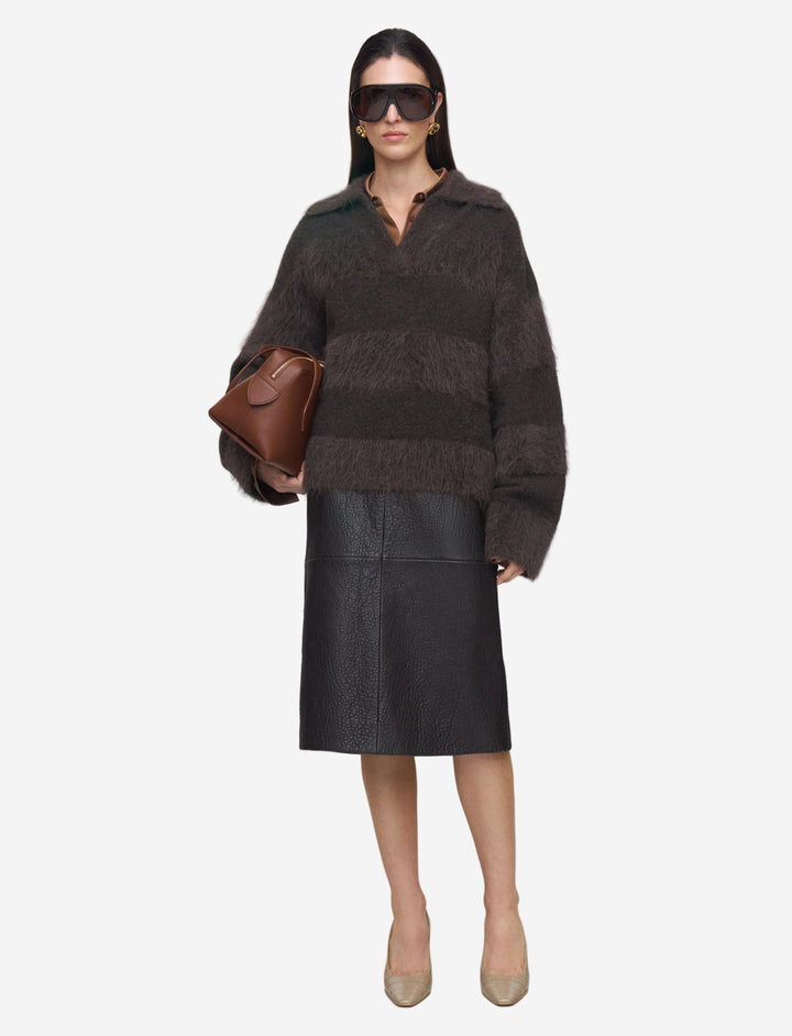 Woman wearing a dark brown sweater and black leather skirt with sunglasses on a white background