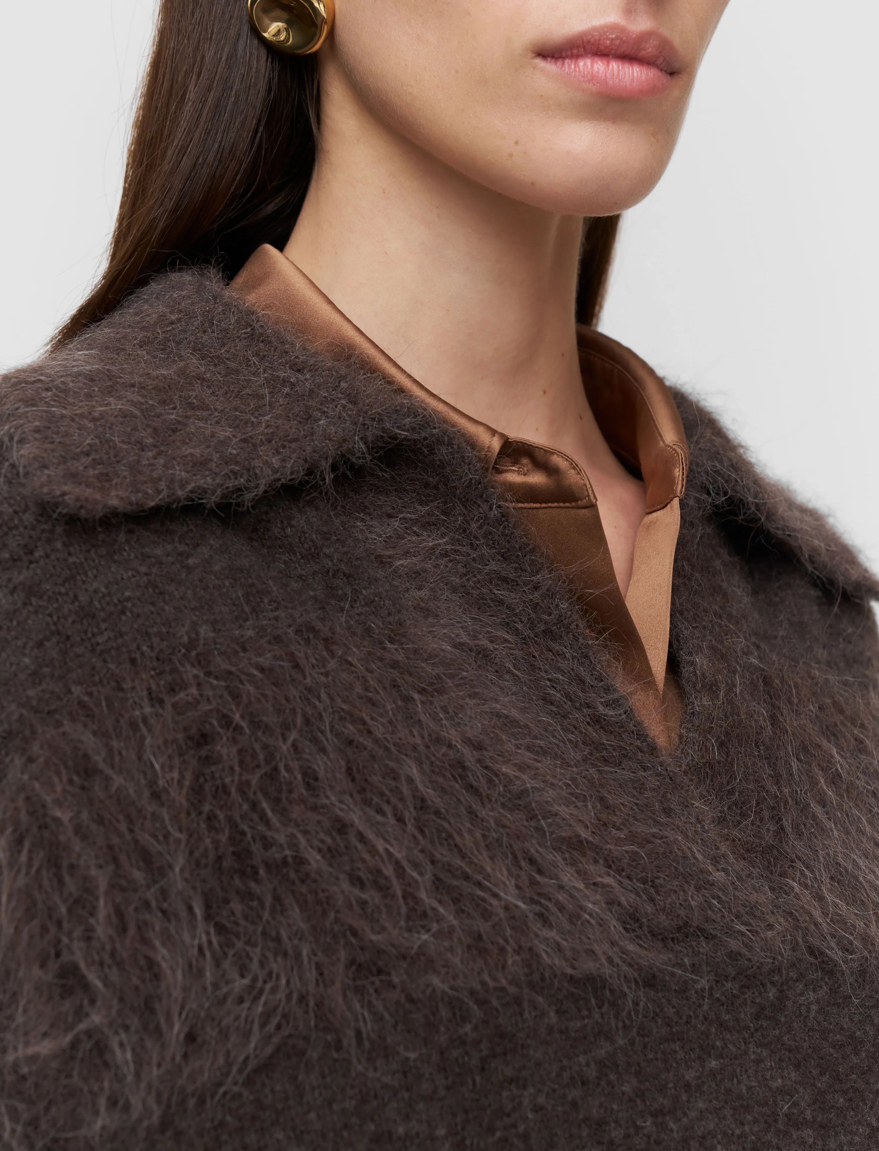 Close-up of a person wearing a brown fur coat with a neutral background