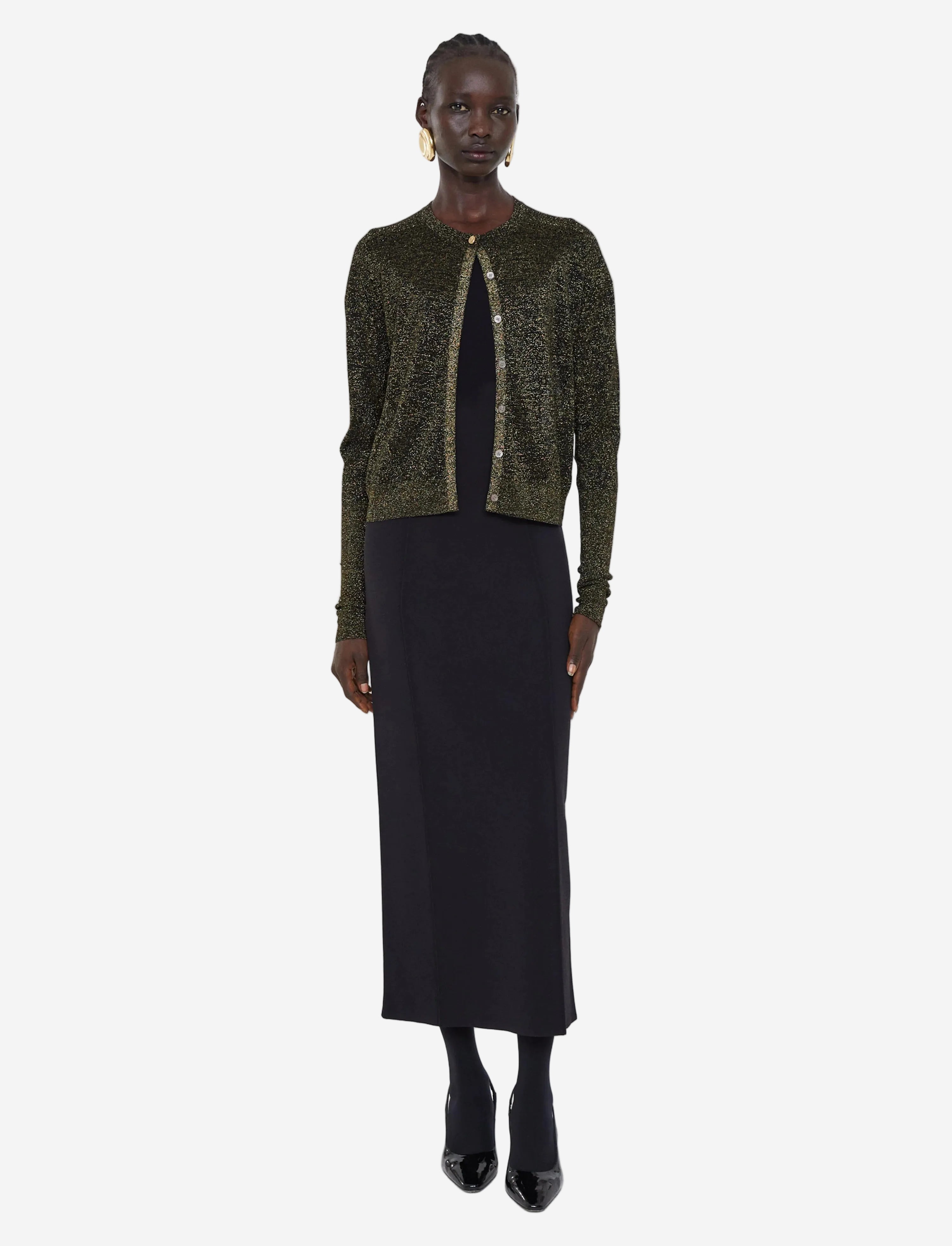 Woman wearing a green sequined cardigan over a black dress on a white background