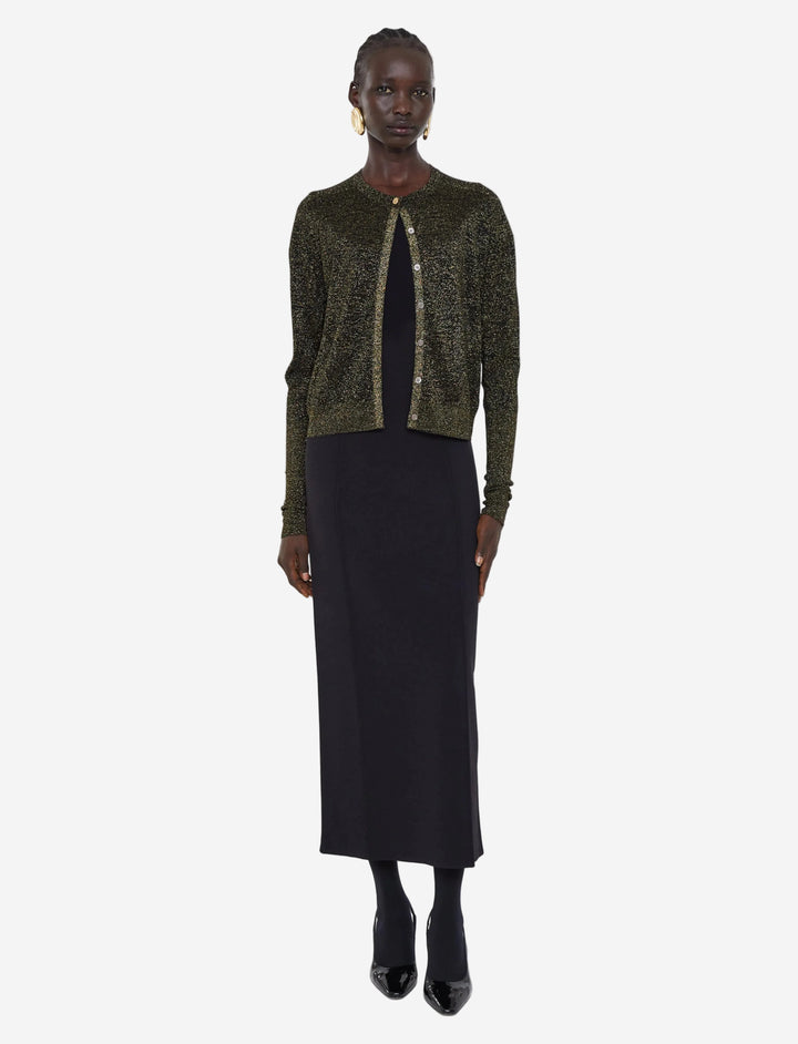 Woman wearing a green sequined cardigan over a black dress on a white background