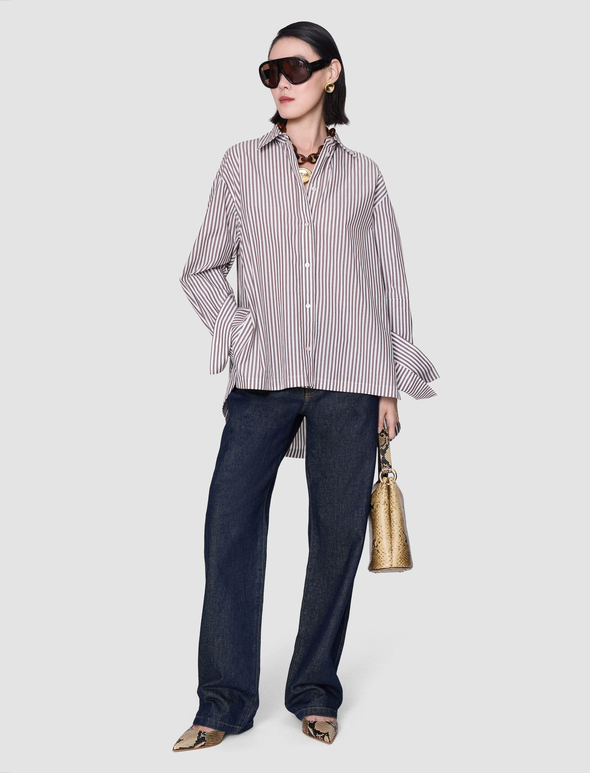A model wearing an oversized grey and white striped shirt with a pointed collar, button front, dropped shoulders, wide cuffs and a longer back hem from Joseph. 