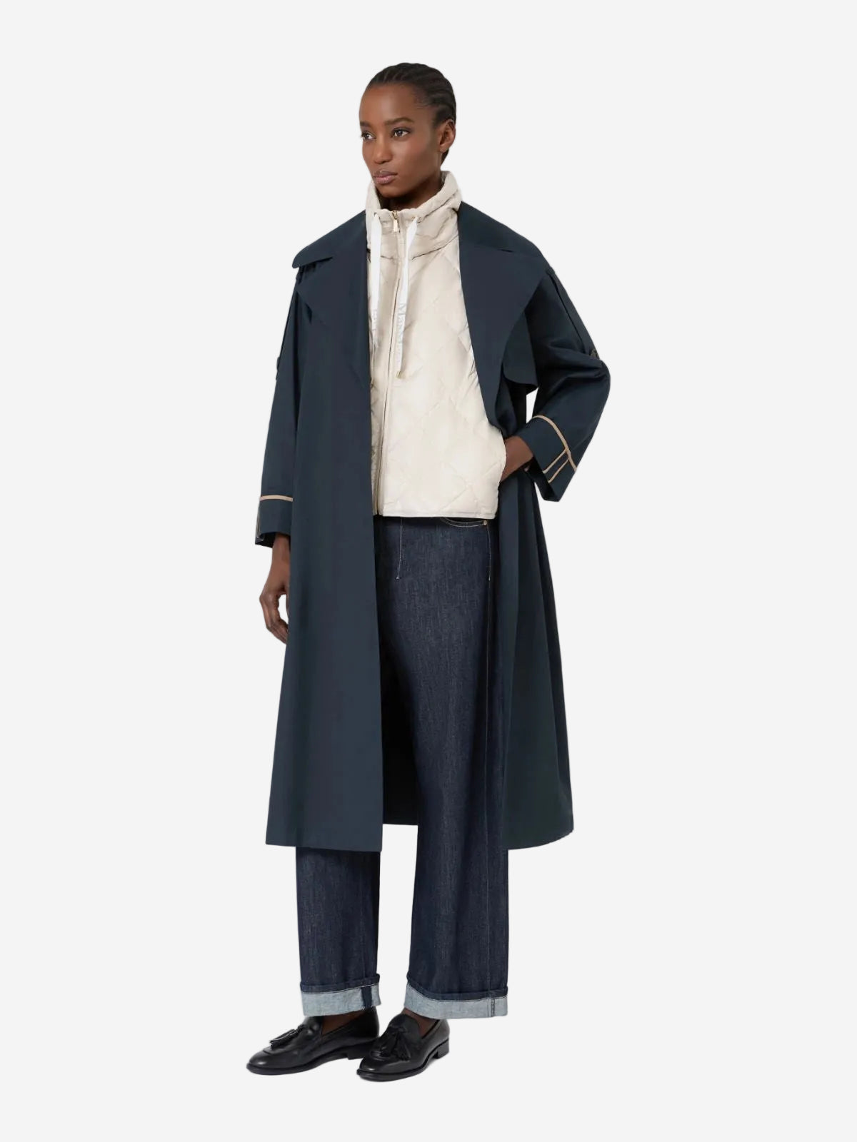 Person wearing a long dark coat over a light sweater and jeans on a white background