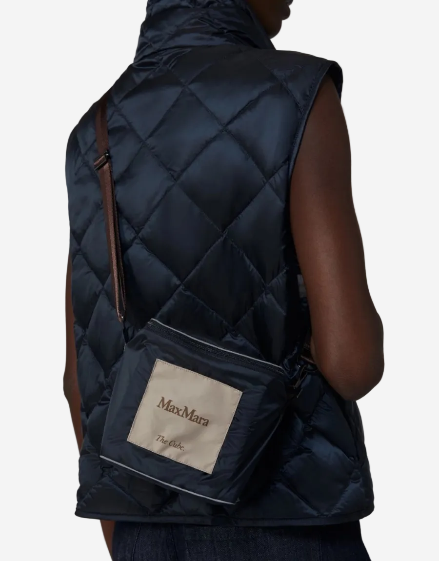 Person wearing a navy quilted vest with a Max Mara backpack on a plain background