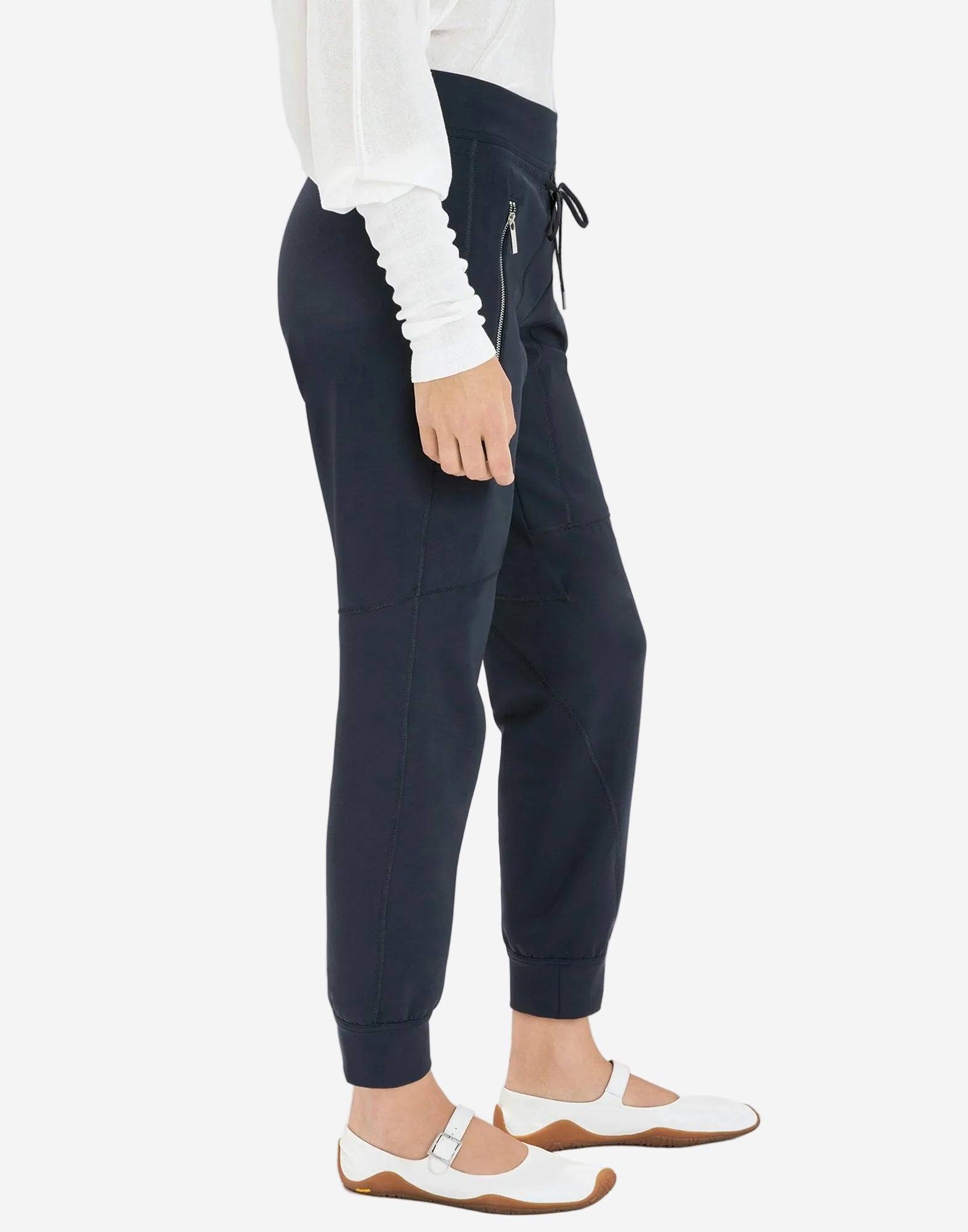 Person wearing navy jogger pants with a white top on a light gray background