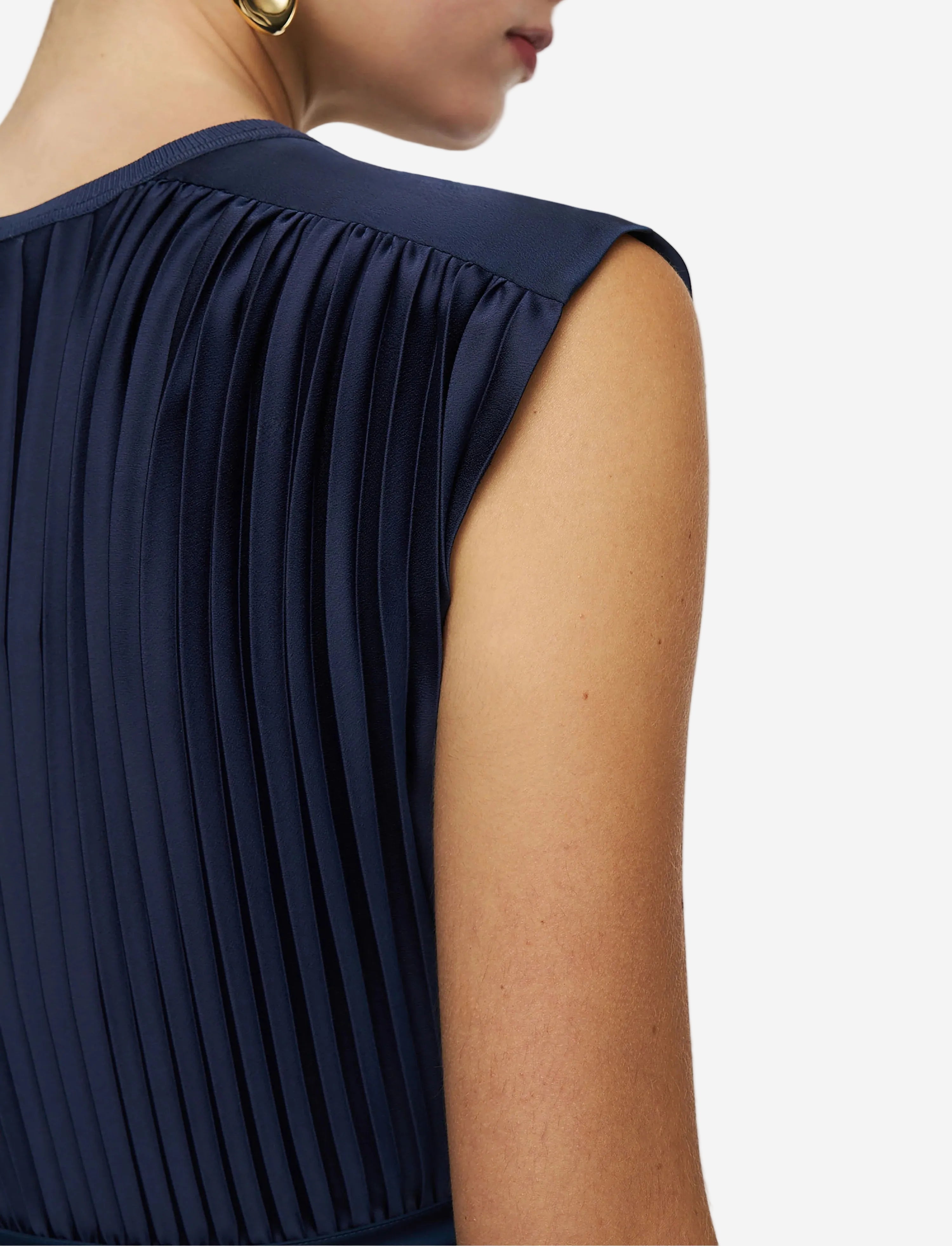 Navy pleated sleeveless top worn by a person on a light gray background