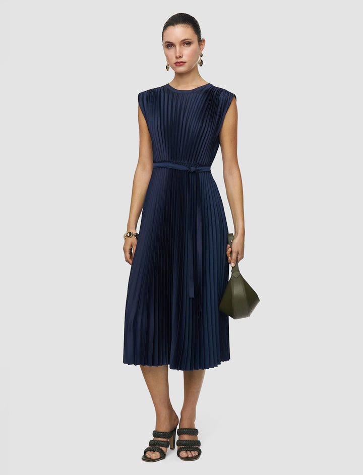 Woman wearing a navy pleated dress holding a green clutch against a light gray background